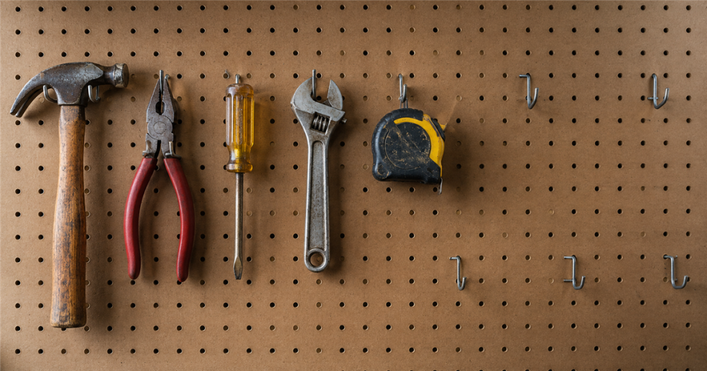 Five purposeful hand tools on a pegboard with empty hooks left unused